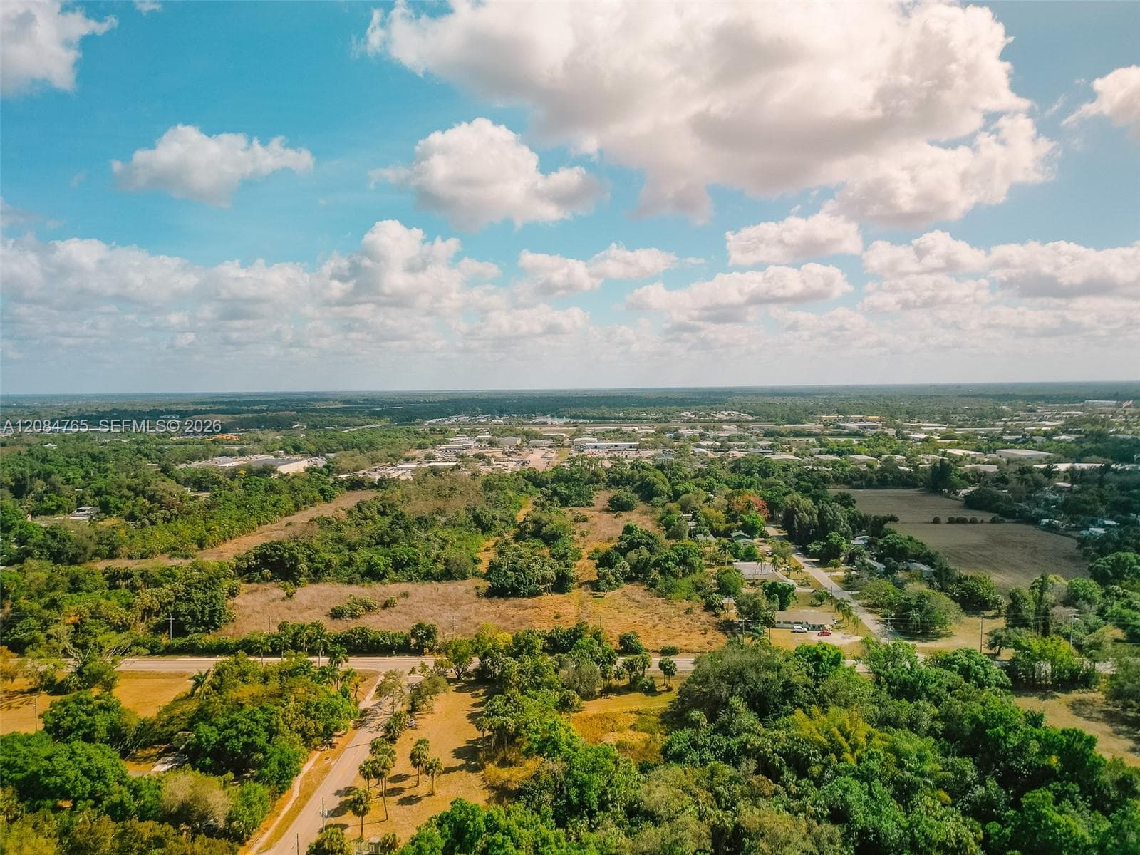 Sweeping drone view under blue skies, highlighting the vacant land's open topography and surrounding natural terrain.